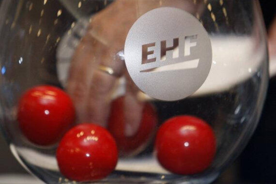 Eine Hand greift in eine Glasschale mit der Aufschrift EHF, in der sich mehrere rote Kugeln befinden, wahrscheinlich als Teil eines Auslosungsverfahrens für ein Sportturnier.
