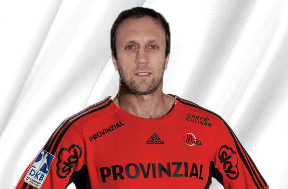 Ein Mann in einem roten Sporttrikot mit schwarzen Akzenten steht vor einem weißen, drapierten Hintergrund. Auf dem Trikot sind das Wort "PROVINZIAL" und mehrere Sponsorenlogos zu sehen.