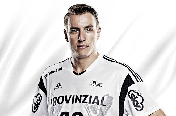 Ein männlicher Sportler in einem weißen Sporttrikot mit schwarzen Akzenten, der vor einem weißen Hintergrund steht. Auf dem Trikot sind das Wort PROVINZIAL und mehrere Logos zu sehen, darunter Adidas und THW Kiel.