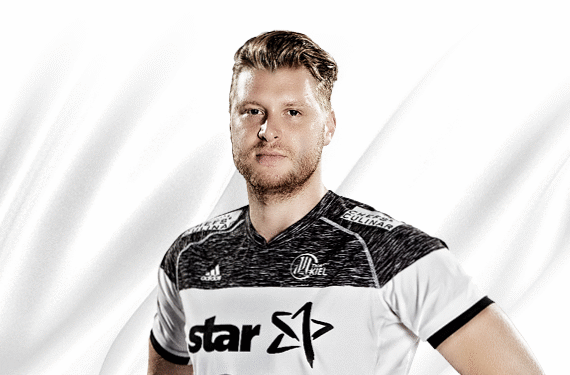 Ein männlicher Sportler mit kurzen blonden Haaren und einem weiß-schwarzen Sporttrikot steht mit den Händen in den Hüften vor einem weißen Hintergrund.