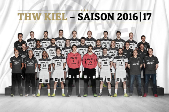 Gruppenfoto der Handballmannschaft und des Stabes des THW Kiel in der Saison 2016-17. Alle tragen Mannschaftstrikots oder Stabskleidung und stehen in Reihen vor einem Hintergrund mit der Aufschrift THW Kiel - Saison 2016|17.