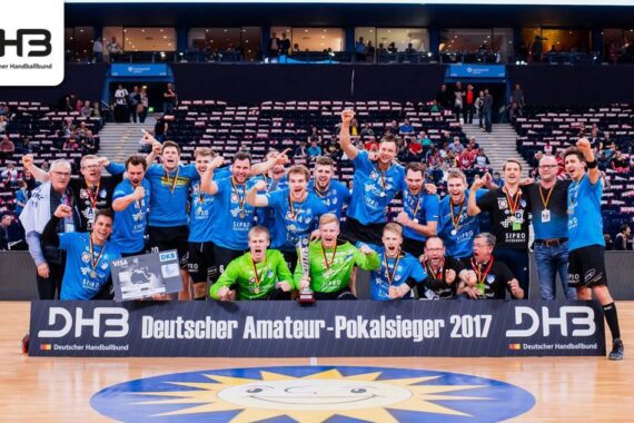 Eine Herren-Handballmannschaft in blauen Trikots feiert den Gewinn des Deutschen Amateur-Pokalsiegers 2017 mit Medaillen und einem Pokal auf einem Hallenplatz, mit jubelnden Fans und einer DHB-Fahne im Hintergrund.