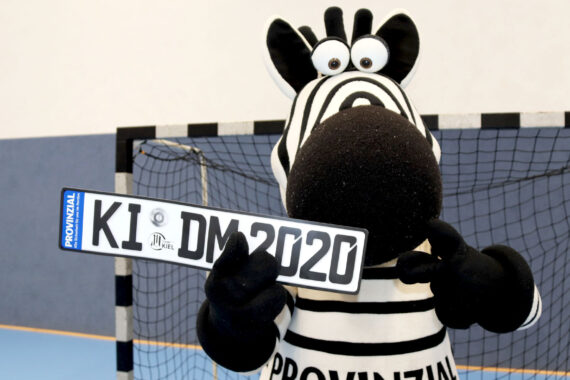 Eine Person im Zebrakostüm steht in einer Halle vor einem Tornetz und hält ein Nummernschild mit der Aufschrift KI DM 2020.