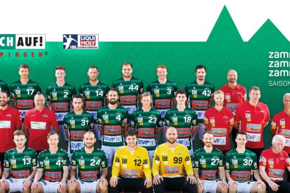 Eine Handballmannschaft in grünen und schwarzen Trikots posiert mit Trainern und Betreuern in roten Hemden. Im Hintergrund sind Mannschaftslogos und der Text zamma.stark. zamma.eins. zamma.wir. mit SAISON 2020/2021 auf der rechten Seite zu sehen.