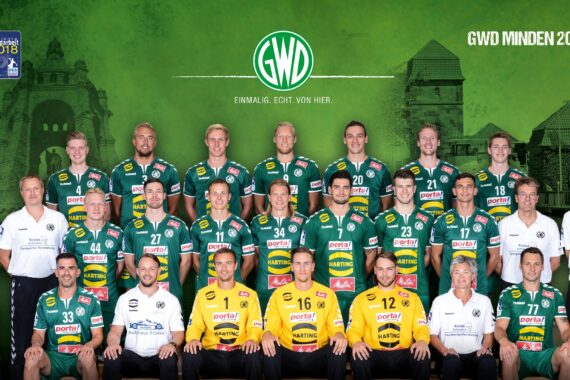 Eine Handballmannschaft in grün-gelb-weißen Trikots posiert für ein Gruppenfoto vor einem grünen Hintergrund mit dem Logo der GWD Minden und dem Text GWD Minden 2018/2019. Es gibt drei Reihen von Spielern und Mitarbeitern.