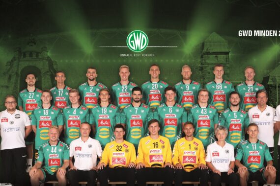 Ein Gruppenfoto der Handballmannschaft von GWD Minden aus der Saison 2019/2020 zeigt die Spielerinnen und Spieler in grünen Trikots und die Betreuerinnen und Betreuer in weißen Hemden in Reih und Glied vor einem grünen, stadionähnlichen Hintergrund mit Teamlogos.
