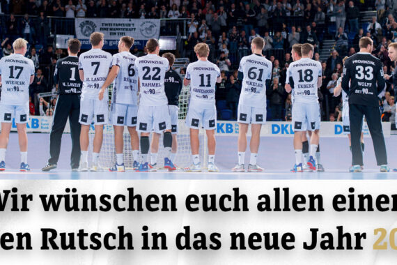 Eine Herrenhandballmannschaft steht in einer Reihe auf dem Spielfeld und blickt auf ein Publikum. Auf einem Banner darunter steht: "Wir wünschen euch allen einen guten Rutsch in das neue Jahr 2019!.