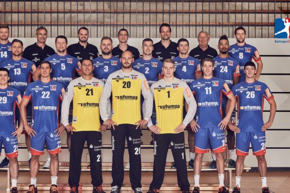 Eine Herren-Handballmannschaft posiert in der Halle in zwei Reihen in blauen Trikots; zwei Spieler in der vorderen Reihe tragen gelbe Torwarttrikots. In der rechten oberen Ecke ist das Logo des HBW Balingen-Weilstetten zu sehen.