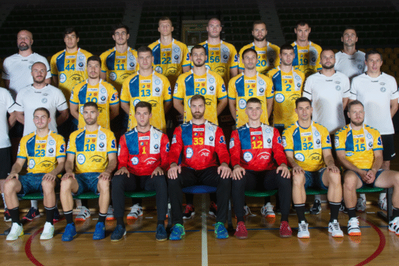 Eine Handballmannschaft in gelben und blauen Trikots stellt sich in der Halle für ein Gruppenfoto auf, vorne sitzen drei Torhüter in roten Trikots. Trainer und Betreuer in weißen Hemden stehen an den Seiten und dahinter.