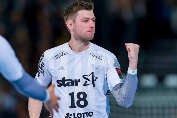 Ein männlicher Handballspieler in einem weißen Trikot mit der Nummer 18 ballt während eines Spiels jubelnd die Faust. Ein anderer Spieler streckt den Arm nach ihm aus. Der Hintergrund ist unscharf, um die Aufmerksamkeit auf den Spieler zu lenken.