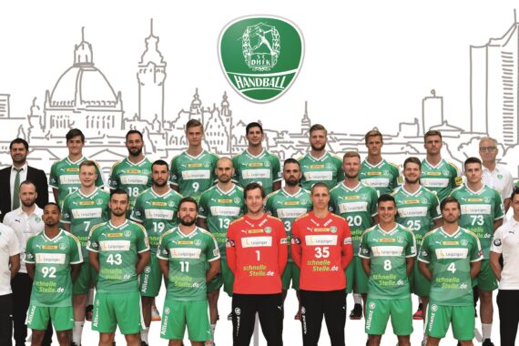 Eine Männerhandballmannschaft in grünen Trikots posiert für ein Gruppenfoto mit Trainern und Betreuern vor einer städtischen Skyline und einem großen Mannschaftslogo. Rechts steht ein Maskottchen.