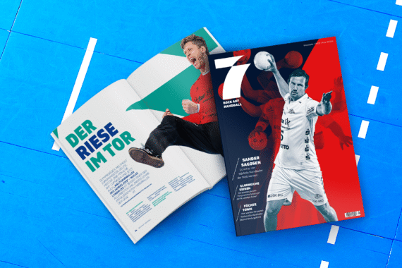 Zwei Handballmagazine liegen auf einem blauen Spielfeld; eines ist aufgeschlagen und zeigt einen jubelnden Mann mit fettgedrucktem deutschen Text, während das andere einen Spieler in Aktion auf einem rot-blauen Cover zeigt.