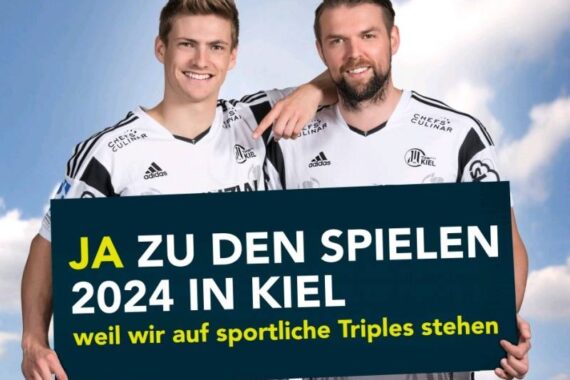Zwei lächelnde Männer in schwarz-weißen Sporttrikots halten ein Schild mit der Aufschrift JA ZU DEN SPIELEN 2024 IN KIEL weil wir auf sportliche Triples stehen vor einem hellblauen Hintergrund.