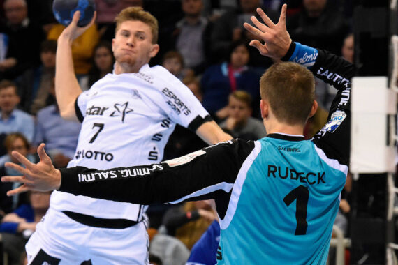 Ein Handballspieler im weißen Trikot bereitet sich darauf vor, den Ball in Richtung Tor zu werfen, während der Torwart im blaugrünen Trikot mit der Aufschrift RUDECK und der Nummer 1 auf dem Rücken die Arme hochreißt, um den Schuss abzuwehren.