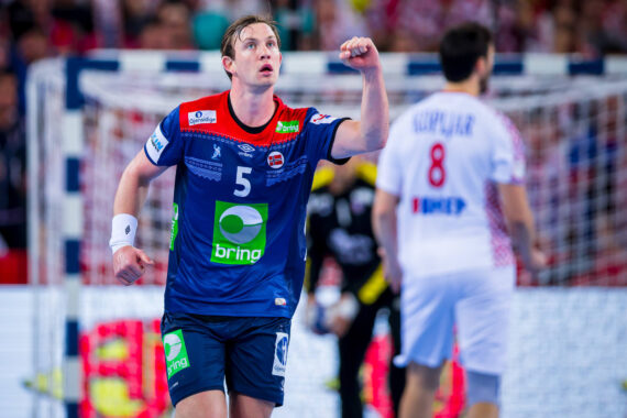 Ein männlicher Handballspieler in einem blau-grünen Trikot mit der Nummer 5 feiert mit erhobener Faust auf dem Spielfeld. Ein anderer Spieler in einem weiß-roten Trikot mit der Nummer 8 ist im Hintergrund zu sehen.