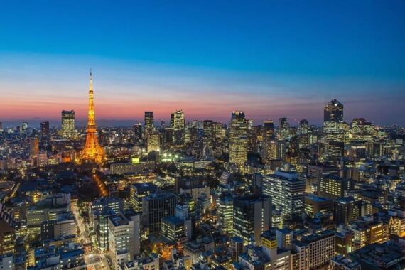 Ein Panoramablick auf Tokio in der Abenddämmerung, mit beleuchteten Gebäuden und dem Tokio Tower, der vor einem farbenfrohen Dämmerungshimmel orange leuchtet.