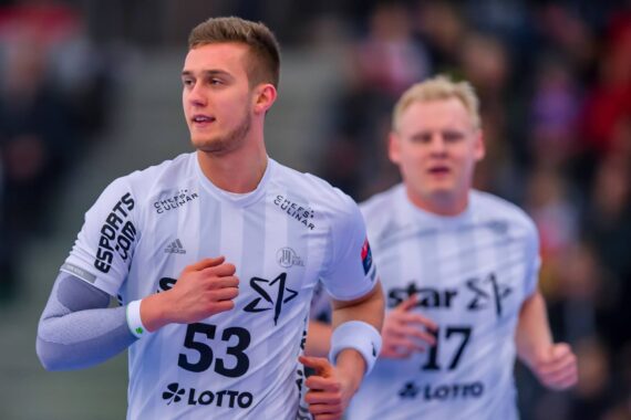 Zwei männliche Handballspieler in weißen Trikots laufen über ein Spielfeld. Der vordere Spieler trägt die Nummer 53, der hintere Spieler die Nummer 17. Auf beiden Trikots sind Logos und Sponsorennamen zu sehen. Der Hintergrund ist unscharf.