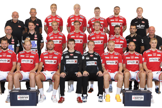 Eine Herren-Handballmannschaft stellt sich in drei Reihen für ein Gruppenfoto auf. Sie tragen passende rote und schwarze Trikots mit verschiedenen Sponsorenlogos. Trainer und Betreuer stehen hinter den Spielern, und zwei große Ausrüstungskästen stehen vor ihnen.