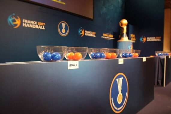 Durchsichtige Schalen, gefüllt mit blauen und orangefarbenen Bällen, stehen auf einem Tisch mit der Aufschrift ROW 6 beim Handballturnier in Frankreich 2017. Im Hintergrund sind die Logos der Veranstaltung und ein Pokal zu sehen.