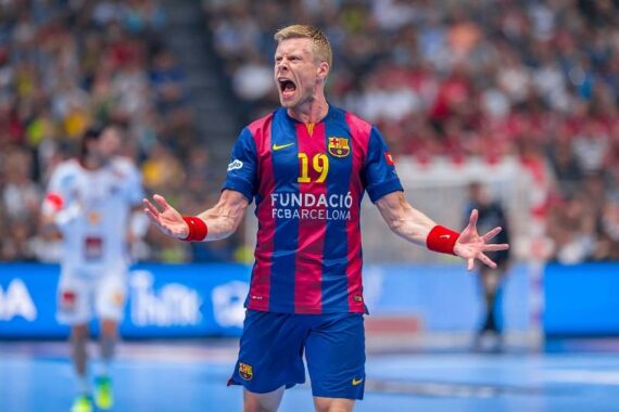 Ein männlicher Handballspieler im blau-roten Trikot des FC Barcelona mit der Nummer 19 schreit während eines Spiels leidenschaftlich mit ausgestreckten Armen. Der Hintergrund zeigt eine unscharfe Halle und andere Spieler.