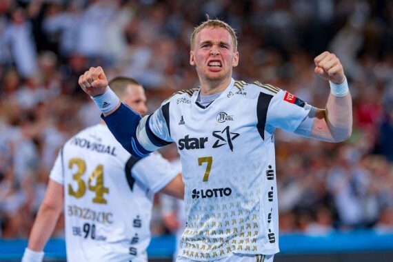 Ein männlicher Handballspieler in einem hellblauen Trikot mit der Nummer 7 ballt beide Fäuste und schreit vor Freude. Ein anderer Spieler mit der Nummer 34 steht in der Nähe mit dem Rücken zur Kamera. Im Hintergrund ist eine jubelnde Menge zu sehen.