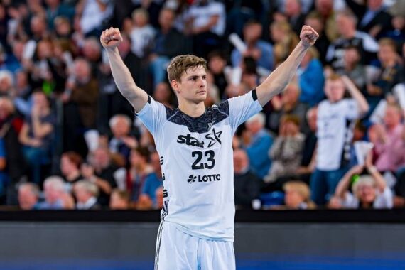 Ein männlicher Handballspieler in einem weißen Trikot mit der Nummer 23 reißt beide Arme jubelnd in die Höhe, während im Hintergrund eine unscharfe Zuschauermenge zu sehen ist.