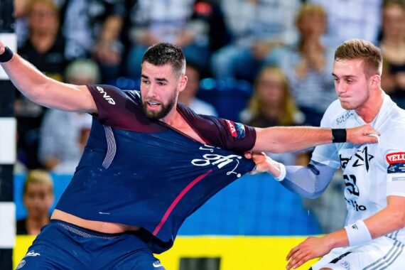 Ein Handballspieler in einem marineblauen Trikot wird während eines intensiven Spiels von einem Gegner in einem weißen Trikot am Hemd gezogen.