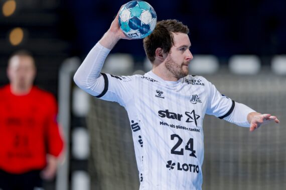 Ein männlicher Handballspieler in einem weißen Trikot mit der Nummer 24 bereitet sich während eines Spiels auf den Wurf eines blau-grünen Handballs vor. Ein Torwart in einem roten Trikot steht im Hintergrund neben dem Tor.