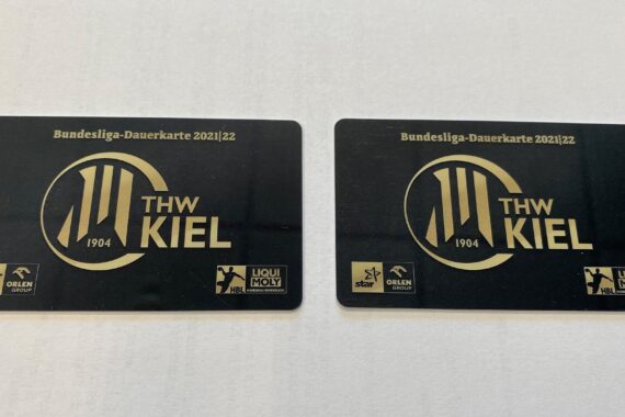 Zwei schwarz-goldene Bundesliga-Dauerkarten des THW Kiel für die Saison 2021/22 liegen nebeneinander auf einer weißen Fläche. Jede Karte zeigt das THW Kiel-Logo und Sponsorenlogos.