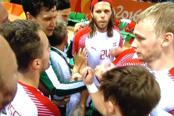Eine Gruppe männlicher Athleten in rot-weißen Trikots drängt sich zusammen, die Hände in der Mitte vereint, um Teamwork und Konzentration zu zeigen, wahrscheinlich während eines Handballspiels bei den Olympischen Spielen 2016.