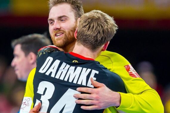 Zwei männliche Sportler in Sporttrikots umarmen sich. Der Sportler, der der Kamera zugewandt ist, lächelt; der andere hat DAHMKE 34 auf dem Rücken. Beide wirken glücklich, was auf eine Feier oder Kameradschaft bei einem Sportereignis hindeutet.