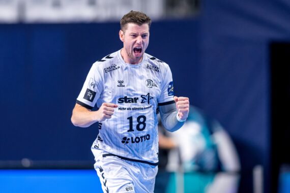 Ein männlicher Handballspieler in einem weißen Trikot mit der Nummer 18 ballt die Fäuste und jubelt auf einem Hallenplatz.