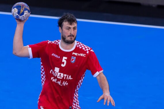 Ein männlicher Handballspieler in einem roten kroatischen Trikot mit der Nummer 5 hält einen Handball in der rechten Hand und bereitet sich auf den Wurf vor. Im Hintergrund ist ein blauer Hallenplatz zu sehen.