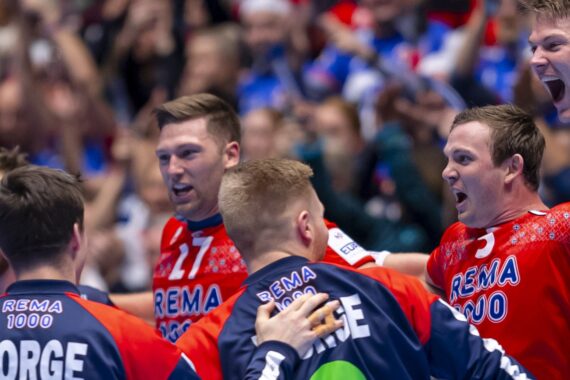 Eine Gruppe männlicher Athleten, die passende rote und blaue Trikots tragen, jubeln während eines Sportereignisses ausgelassen, umarmen sich gegenseitig und machen dabei begeisterte Gesichter. Die Menge ist im Hintergrund verschwommen.