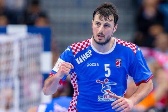 Ein männlicher Handballspieler in einem blauen Trikot der kroatischen Nationalmannschaft mit rot-weiß karierten Schultern hebt während eines Spiels die Faust. Das Trikot trägt die Nummer 5 und das Logo der EHF Euro Croatia 2018.