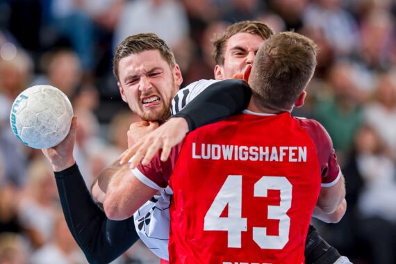 Ein Handballspieler in einem weißen Trikot wird von einem Spieler in einem roten Trikot mit der Aufschrift Ludwigshafen 43 verteidigt, wobei beide Spieler während eines Spiels großen Einsatz zeigen. Der weiße Ball wird gut festgehalten.