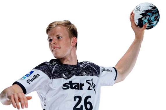 Ein männlicher Handballspieler in einem weiß-schwarzen Trikot mit der Nummer 26 bereitet sich darauf vor, einen Ball zu werfen. Er ist konzentriert, hebt den rechten Arm und hält den Ball in der Hand vor einem weißen Hintergrund.