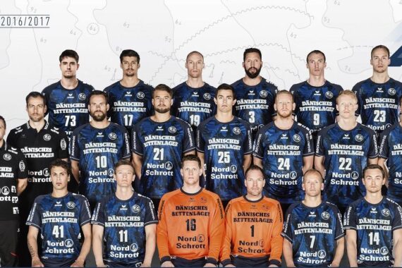 Eine Handballmannschaft der Männer posiert für ein Gruppenfoto in passenden blauen Trikots mit Sponsorenlogos. Zwei Spieler in orangefarbenen Torwarttrikots sitzen in der ersten Reihe. Die Mannschaft ist aus der Saison 2016/2017.