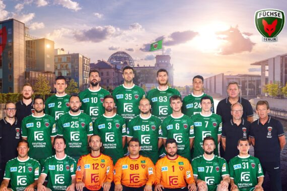 Eine Handballmannschaft in grünen und orangefarbenen Trikots posiert für ein Gruppenfoto im Freien mit städtischen Gebäuden, einem Fluss und dem Reichstag im Hintergrund. Die Logos der Füchse Berlin und der HBL Liqui Moly befinden sich in der oberen rechten Ecke.