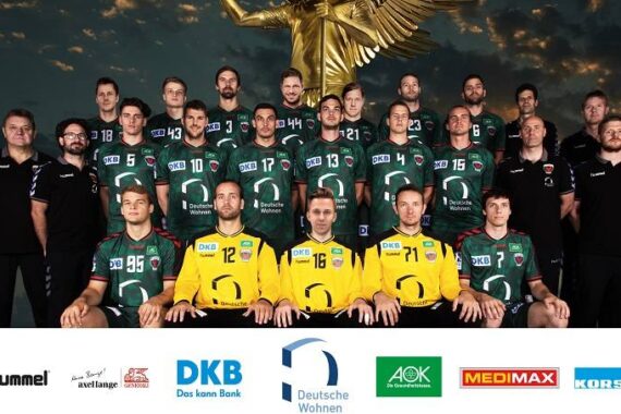 Eine Handballmannschaft der Männer posiert für ein Gruppenfoto in grün-schwarzen Trikots mit drei Spielern in Gelb, die vor einer Statue mit Sponsorenlogos am unteren Rand stehen.