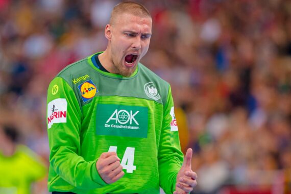 Ein männlicher Handballspieler in einem grünen Trikot mit der Nummer 44 scheint während eines Spiels mit geballten Fäusten leidenschaftlich zu schreien und zu feiern. Der Hintergrund zeigt eine unscharfe Menge und einen anderen Spieler.