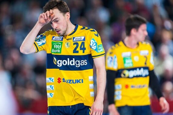 Ein Handballspieler in einem gelb-blauen Trikot mit der Nummer 24 wischt sich den Schweiß von der Stirn und sieht müde aus. Ein anderer Spieler in einem ähnlichen Trikot ist unscharf im Hintergrund zu sehen.