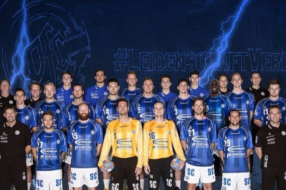 Eine Herren-Handballmannschaft in blau-weißen Trikots posiert für ein Gruppenfoto mit Trainern und Betreuern vor einem blauen Hintergrund mit dem Hashtag "LEIDENSCHAFTVEREINT".