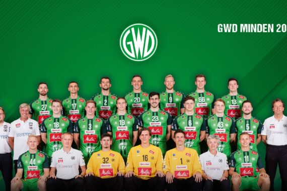 Gruppenfoto der GWD Minden Handballmannschaft 2020/2021, mit Spielern in grünen Trikots und Mitarbeitern in weißen Hemden, alle posieren vor einem grünen Hintergrund mit dem GWD-Logo und dem Text GWD Minden 2020/2021.