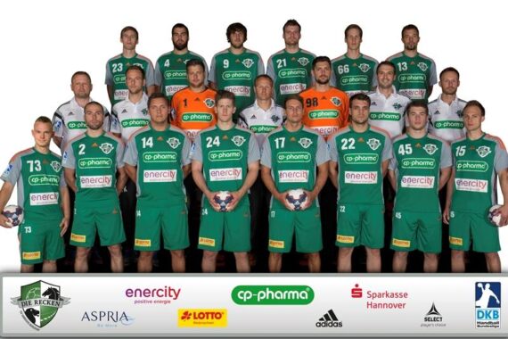 Eine Herren-Handballmannschaft in grünen Trikots posiert in drei Reihen mit ihren Trainern und hält Handbälle in der Hand. Vor ihnen ist ein Banner mit verschiedenen Sponsorenlogos zu sehen.