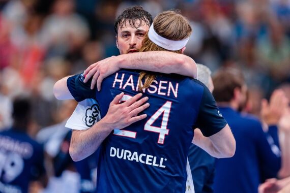 Zwei männliche Handballspieler umarmen sich nach einem Spiel. Auf dem Trikot eines Spielers steht Hansen 24 und Duracell. Die Szene suggeriert Sportlichkeit und Kameradschaft in einer Halle.