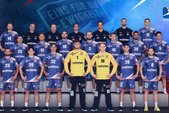 Eine Herren-Handballmannschaft in blauen und gelben Trikots posiert für ein Gruppenfoto mit den Trainern, stehend und kniend in Reihen vor einem blau-roten Hintergrund mit dem HBW-Logo.