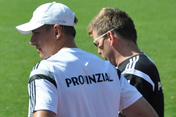 Zwei Männer stehen im Freien auf grünem Gras, beide tragen Sporttrikots mit der Aufschrift PROVINZIAL auf dem Rücken. Einer trägt eine weiße Mütze und ein weißes Hemd, der andere eine Sonnenbrille und ein schwarzes Hemd mit weißen Streifen.