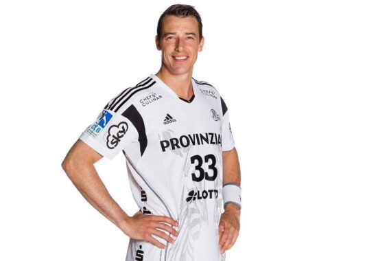 Ein männlicher Sportler in einem weißen Sportdress mit der Nummer 33, der mit einer Hand in der Hüfte steht und lächelt, isoliert auf weißem Hintergrund.