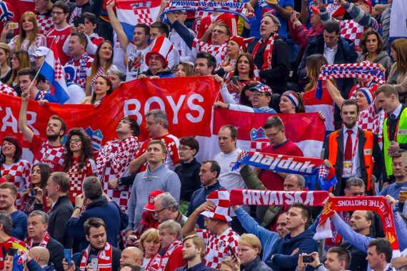 Eine große Menge begeisterter Fußballfans, meist in rot-weiß karierter Kleidung, schwenkt Fahnen, Banner und Schals und jubelt leidenschaftlich in einem Stadion.
